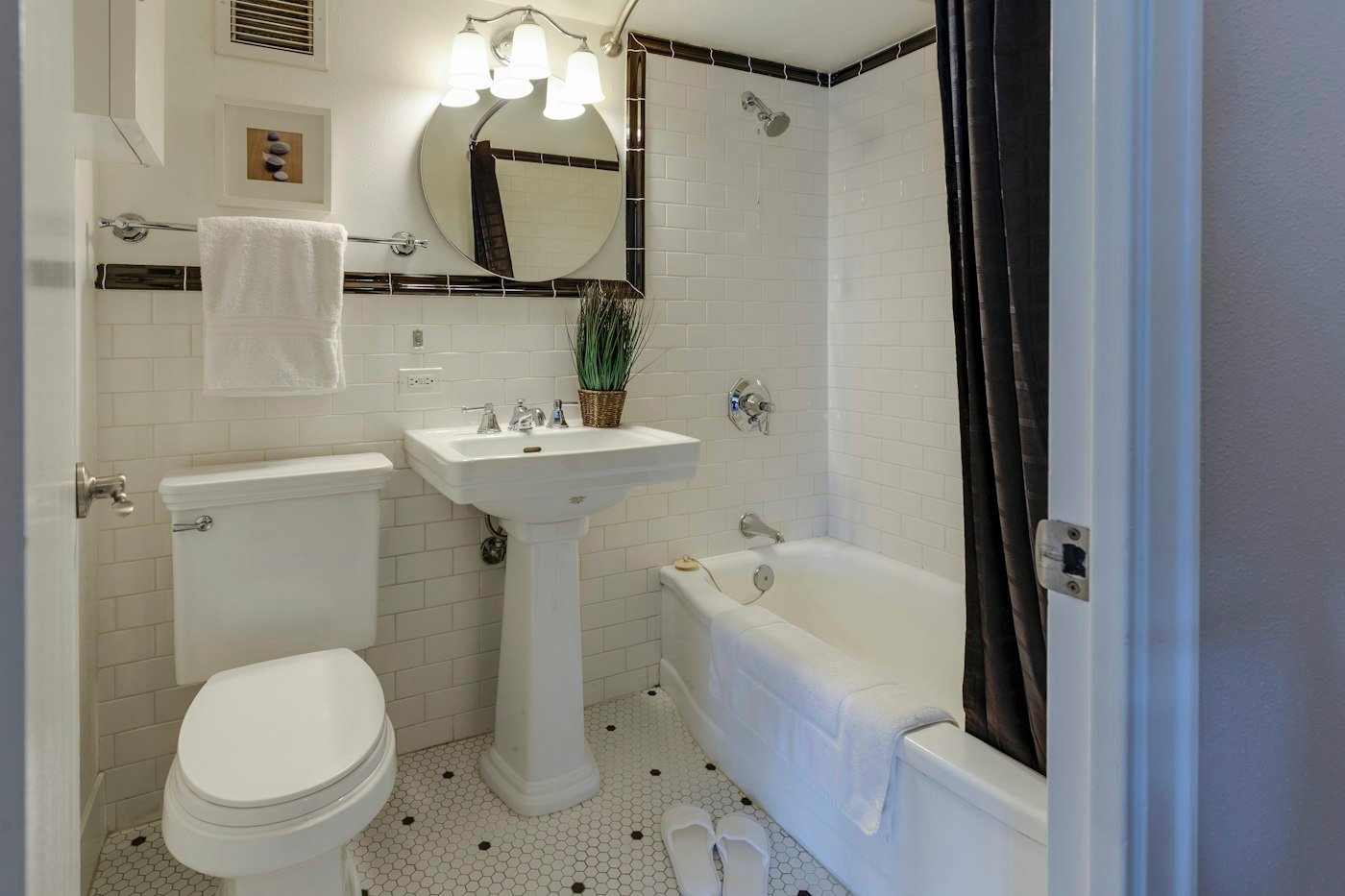 A white bathroom with a pedestal sink, a toilet, a bath, and a round mirror