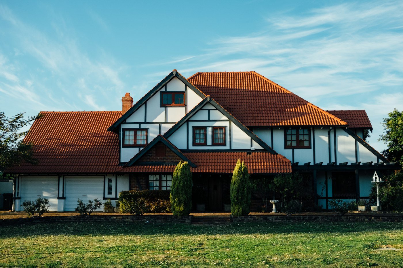 A white house with black timber beams, a red tiled roof, a white garage door, and a lawn in front