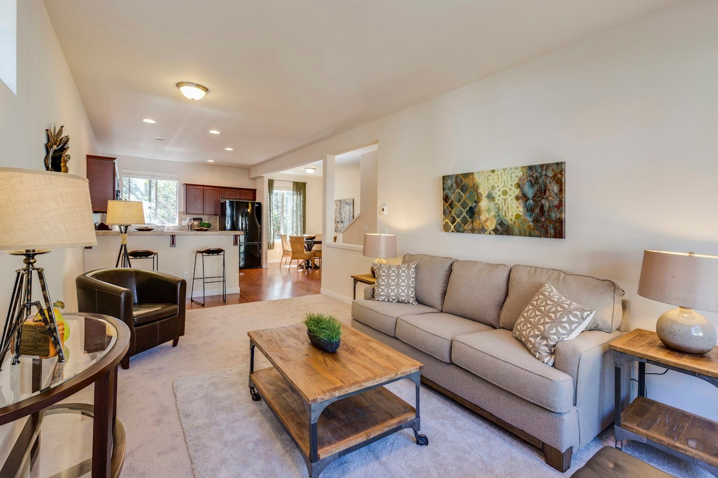 A beige sofa, a wooden coffee table on a pale rug, and a view through to a kitchen